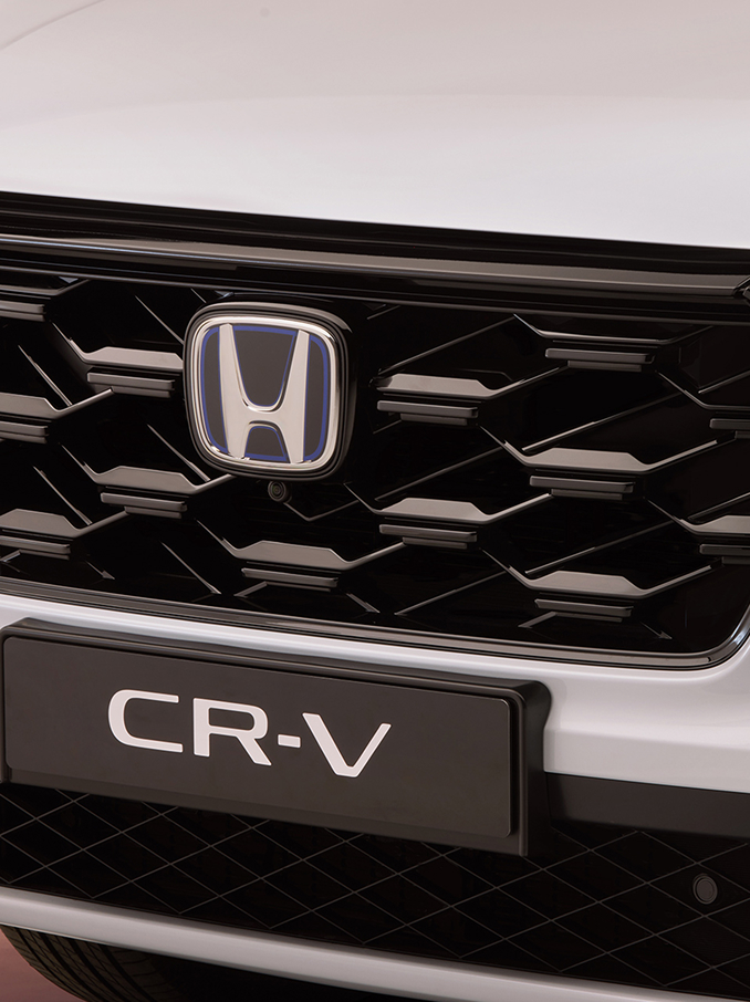Detailný záber na prednú mriežku chladiča modelu Honda CR-V s čiernym vzorom včelieho plástu, logom Honda v strede a názvom modelu CR-V viditeľným pod ním.