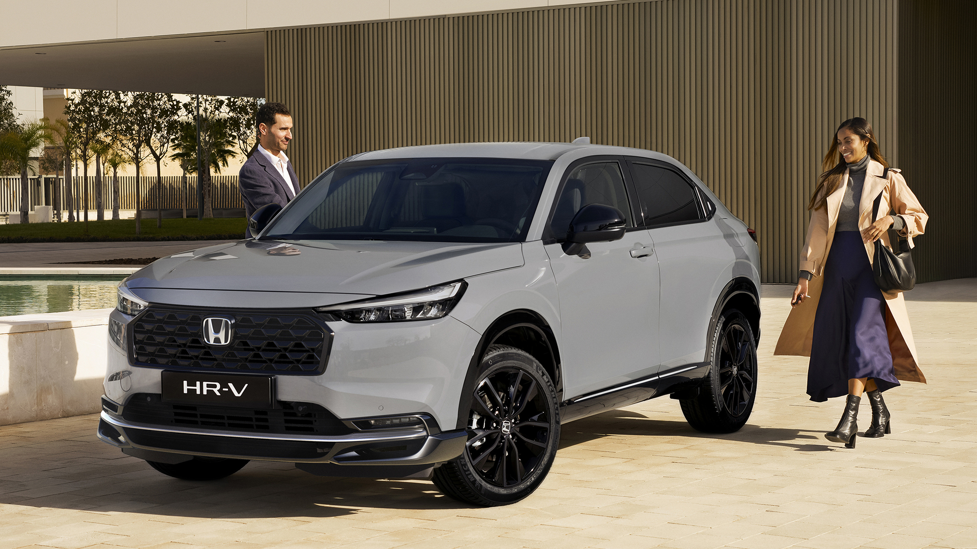 Biela Honda HR-V jazdí ku kamere po dvojpruhovej ceste, obklopená vysokou zlatou trávou pod modrou oblohou.