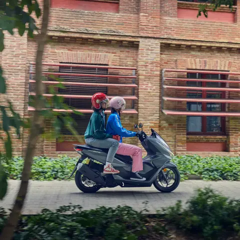 Bočný záber na figurantov pri jazde na motocykli PCX125 v meste.